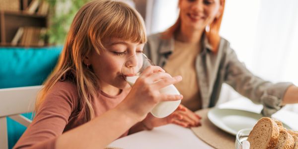 Girl drinking milk with smiling woman in the background.