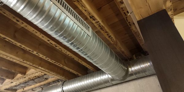 Exposed metal HVAC ductwork under a wooden ceiling.