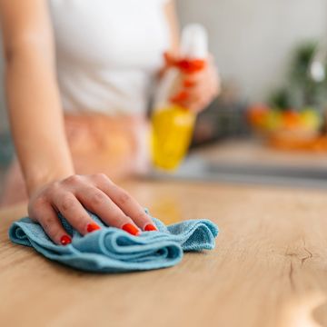 A person cleaning a wooden surface with a blue cloth.