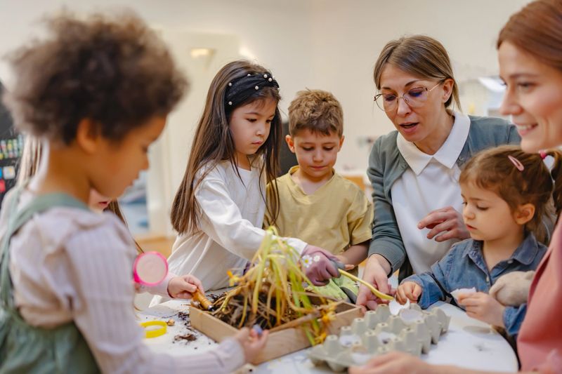 Group of diverse preschool children learning gardening with teachers, exploring soil and plants in a fun, hands-on classroom activity