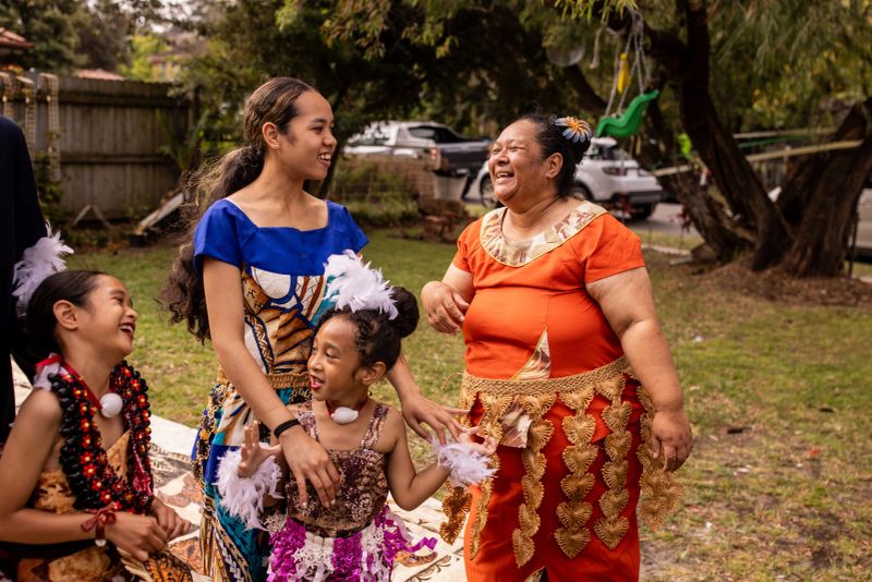 Large Pacific Islander family, spanning several generations, together in their backyard, all wearing traditional clothing.