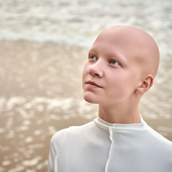 Young bald person looking upward near water.