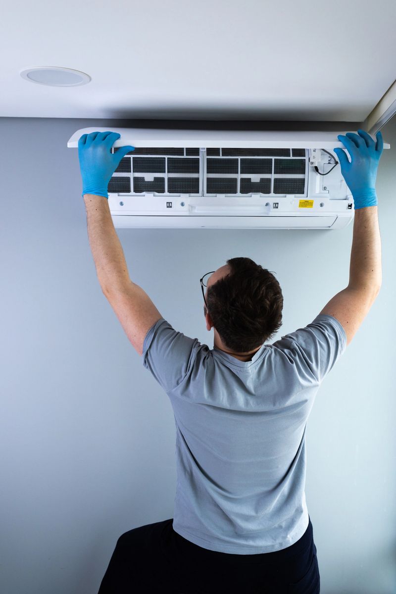 A technician wearing blue gloves is carefully servicing an air conditioning unit mounted on the wall, showcasing the importance of proper maintenance and safety during HVAC repairs.