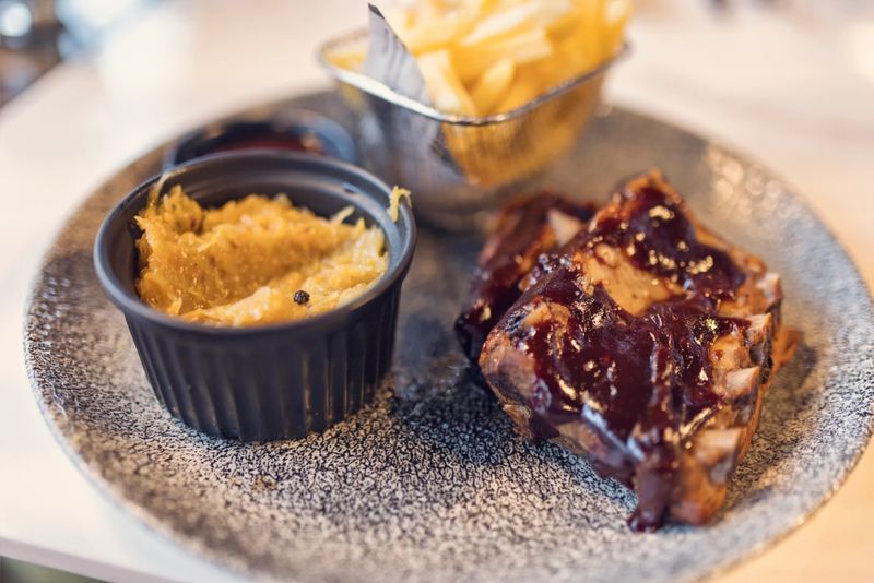 Hearty meal featuring tender ribs generously coated with barbecue sauce, arranged on a speckled gray plate. Alongside the ribs, a small basket holds golden, crispy French fries and a black bowl is filled with sauerkraut, garnished with peppercorns.
Shot with Canon R5
