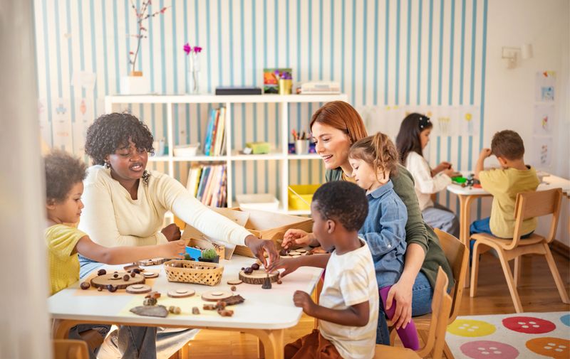 Preschool teacher guides a diverse group of children in a natural materials activity in a bright, creative classroom setting focused on hands-on learning.