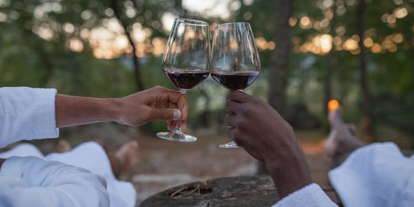 Two people clinking glasses of red wine outdoors at sunset.