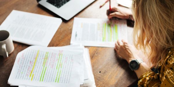 Women reviewing documentation on a wood desk with laptop away from papers.