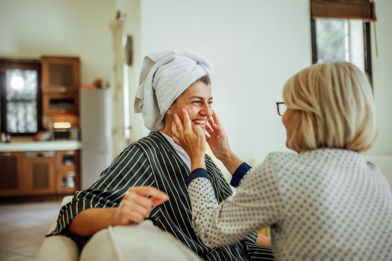 A mother and daughter smile while applying skincare products together at home, enjoying quality time during their beauty routine