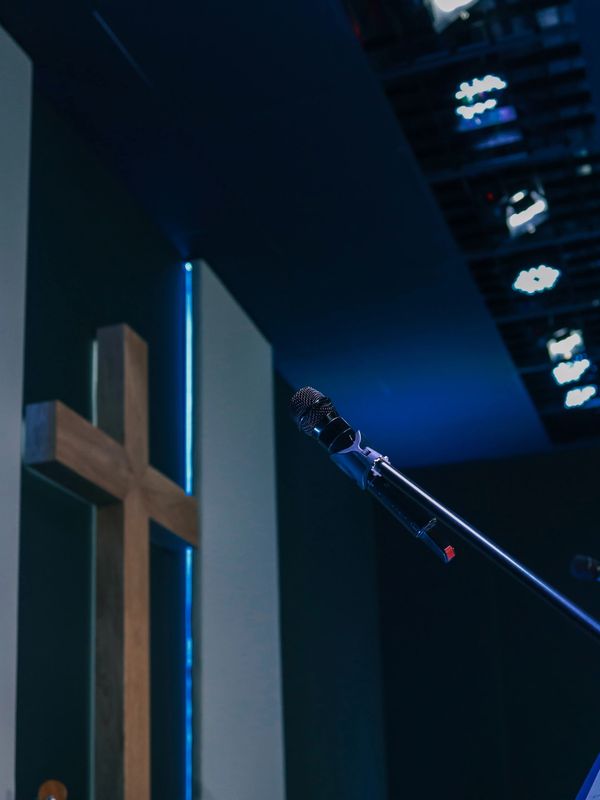 Microphone and music stand in a modern church setting with a wooden cross.