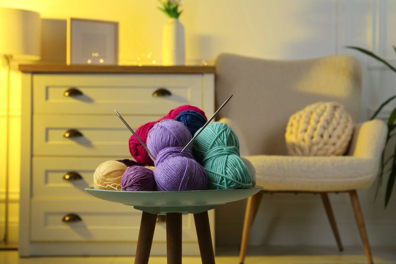 Colorful yarns and knitting needles on coffee table in cozy room