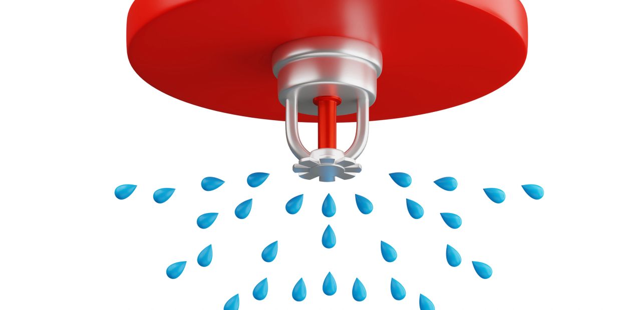 Close-up of a red fire sprinkler spraying water droplets.