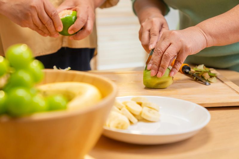 Group of Happy Asian senior women having breakfast together at home. Elderly retired woman friends enjoy healthy lifestyle making homemade greek yogurt with mixed fruit, nuts and honey in the kitchen.