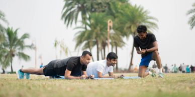 Three men exercising outdoors on a grassy field near palm trees.