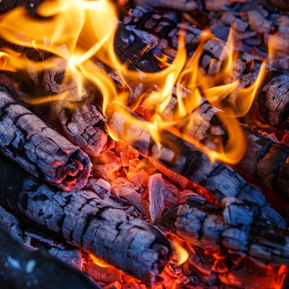 Close-up of glowing embers and bright flames on burning logs.