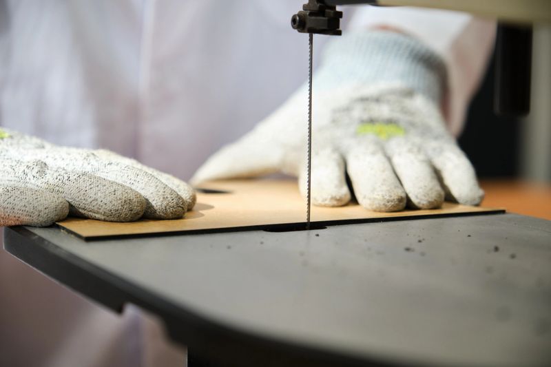 Un artisan utilise une scie à ruban pour couper une feuille de contreplaqué, portant soigneusement des gants de sécurité pour assurer une menuiserie précise.