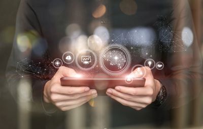 Person holding smartphone with digital technology icons floating above.