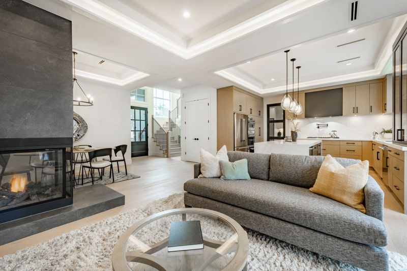 spacious living room in a newly constructed home staged professionally with fireplace view to kitchen grey sofa area rug built in cabinets and shelving recessed lighting in the ceiling modern new furniture