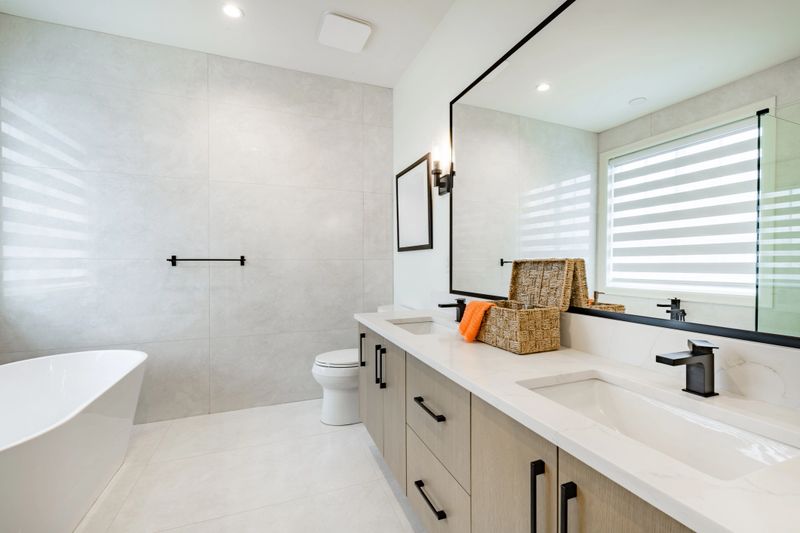Newly built home bathroom interior primary or master bath with glass wall shower white marble granite floors and countertops large windows with blinds covering free standing bathtub sinks black fixtures bright spacious modern