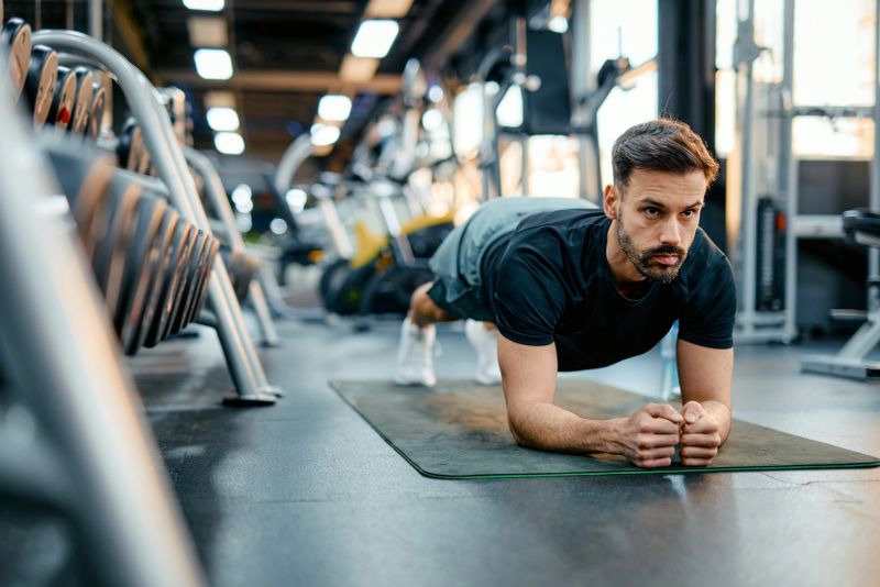 Young sportsman performing a plank exercise during an intense workout in a modern gym, showcasing dedication and strength while maintaining perfect form and focus