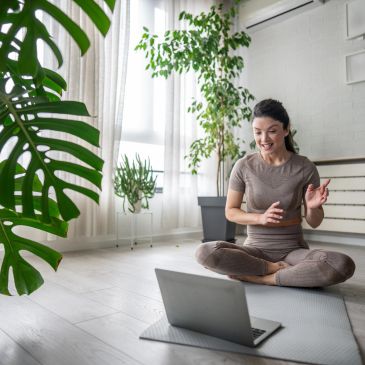 Woman doing yoga while video chatting on laptop.