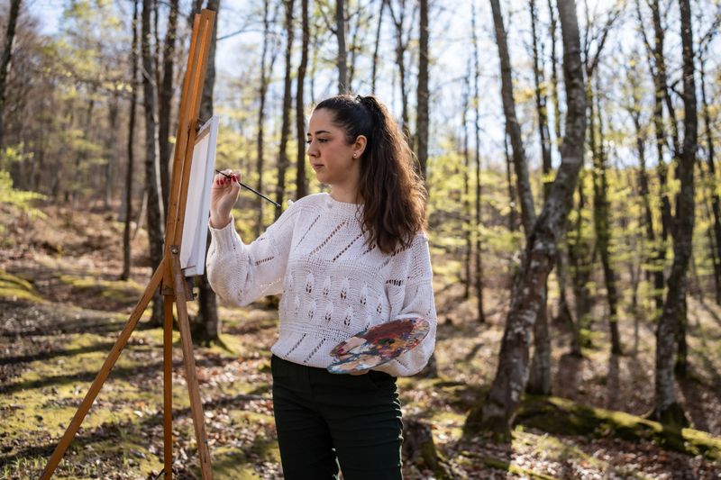 A talented artist paints on a canvas in a peaceful forest, surrounded by vibrant foliage and natural beauty. This scene captures the harmony of creativity and nature.