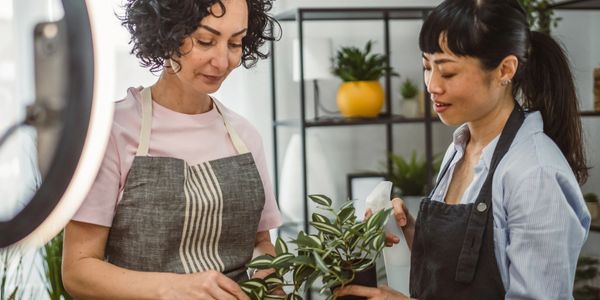 Two women tending to potted plants indoors, wearing aprons.