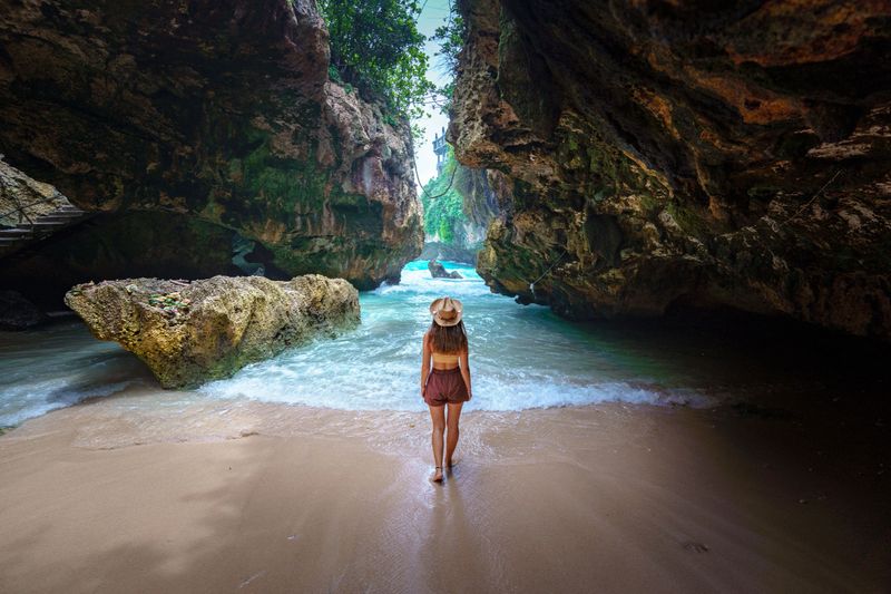 Back of girl traveler wearing hat on the beach among the rocks on Bali island. Journey to a beautiful destination