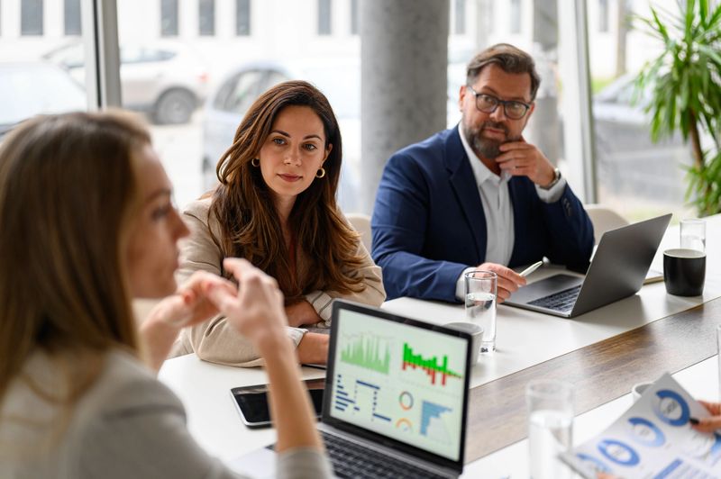 Female executive discussing financial report with businessman and businesswoman in board room during meeting