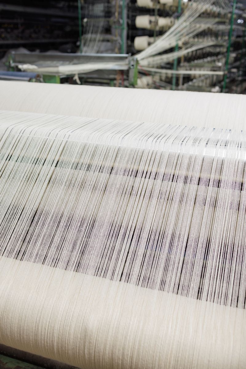 Automated textile production with white threads on a weaving loom machine in a modern fabric manufacturing plant.