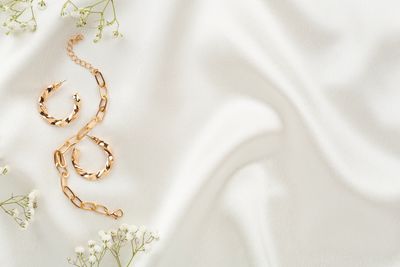 Gold chain bracelet and hoop earrings on white fabric with small flowers.