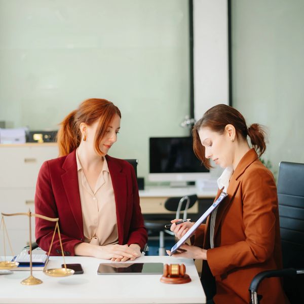 Two women in professional attire discussing documents in an office setting