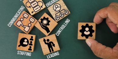 Wooden blocks labeled with management functions held by a hand on a green background.