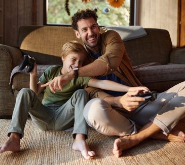 Father and son joyfully playing video games together on the floor.