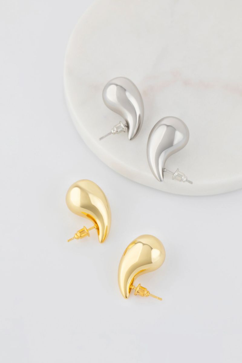 Elegant gold and silver droplet earrings resting on marble surface. Catalog of jewelry