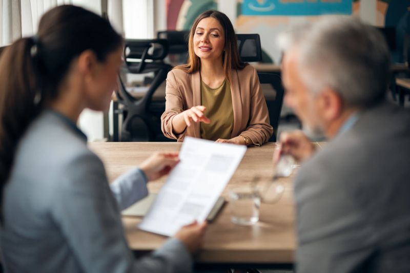 A professional woman attends an interview with a recruitment panel in a modern office setting.