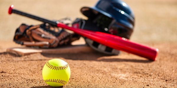 Softball with bat, helmet and glove on the ground.