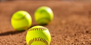 Three softballs on dirt field focused on the nearest ball.