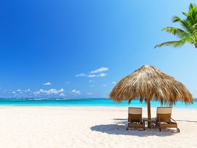 Two beach chairs under a straw umbrella on a sandy beach.