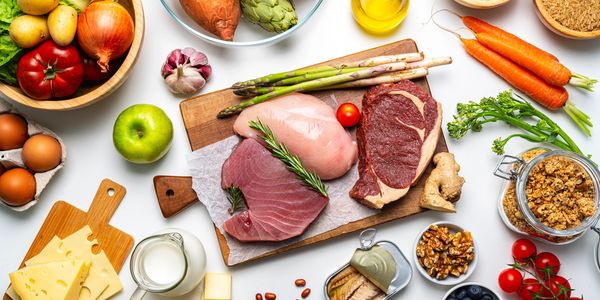 A variety of fresh meats, vegetables, fruits, and dairy arranged on a white surface.