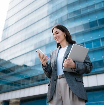 Young professional woman smiling while using smartphone outdoors.
