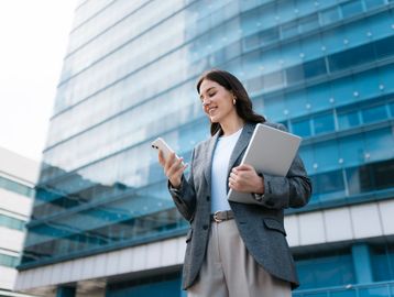 Young professional woman using phone outside a modern office building.
