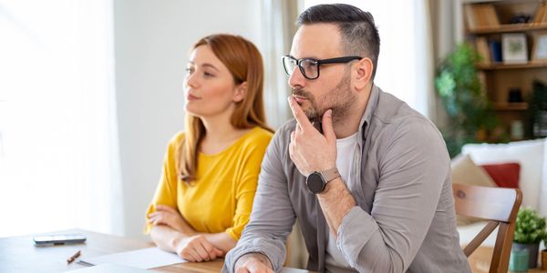 A man and woman sitting at a table, appearing thoughtful and distant.