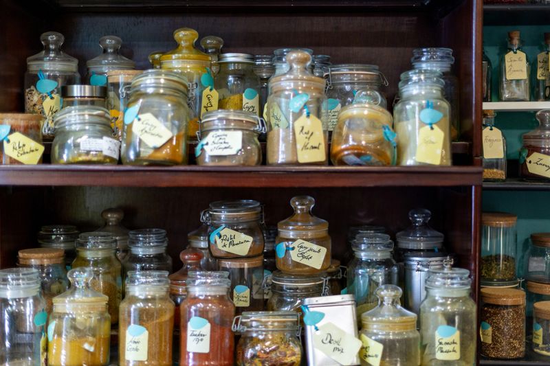 Glass jars filled with colorful spices and herbs, neatly organized on wooden shelves, creating a vibrant and aromatic display