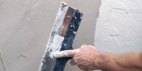 Hand smoothing plaster on wall with a trowel.