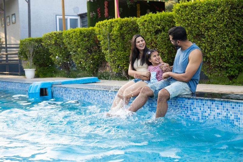 Young indian family enjoy at swimming pool in summer holiday, India parents with child daughter having fun relaxing together at hotel resort vacation. Bonding and togetherness