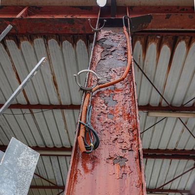 Rusty metal column with peeling paint and electrical cables under a corrugated roof.