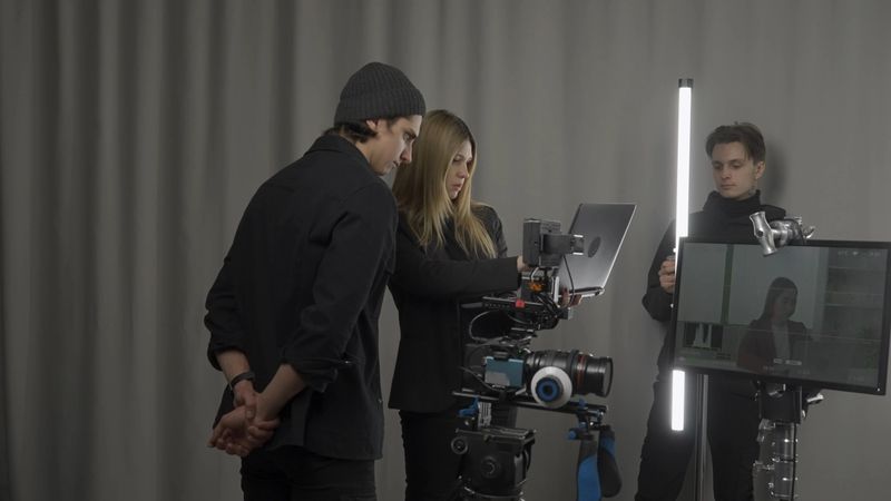 The crew backstage. Female director, camera operator and lighting technician in the studio during filming. The lighting technician adjusts the lighting, filmmaker and cameraman look at shooting plan.