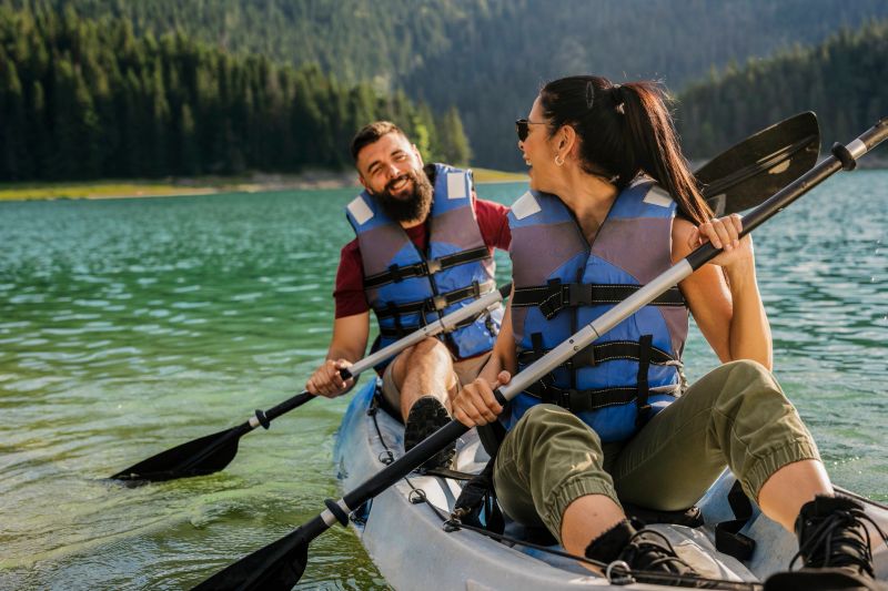 Happy couple wearing life jackets paddles a kayak on a serene mountain lake, enjoying the tranquility and beauty of nature during their summer vacation