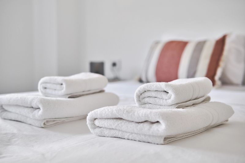 Close up of freshly folded white towels placed on neatly made bed in modern, minimalistic bedroom. A cozy, welcoming setup ideal for hospitality, hotel, or spa-themed visuals, no people