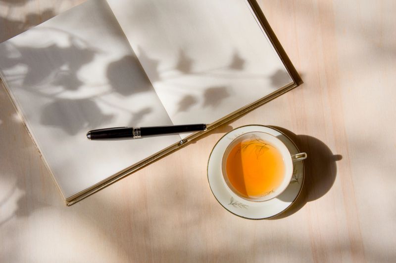 Tea in porcelain cup and journal on wooden table, part of mental health routine - journal for therapy session - concepts and ideas, healthy lifestyle